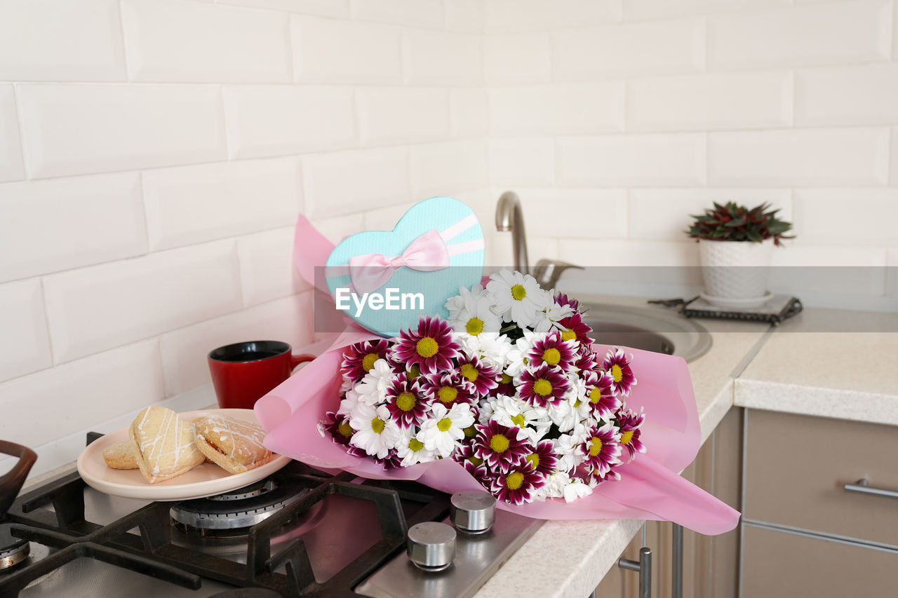 Bouquet of spring flowers on kitchen table with gift box.