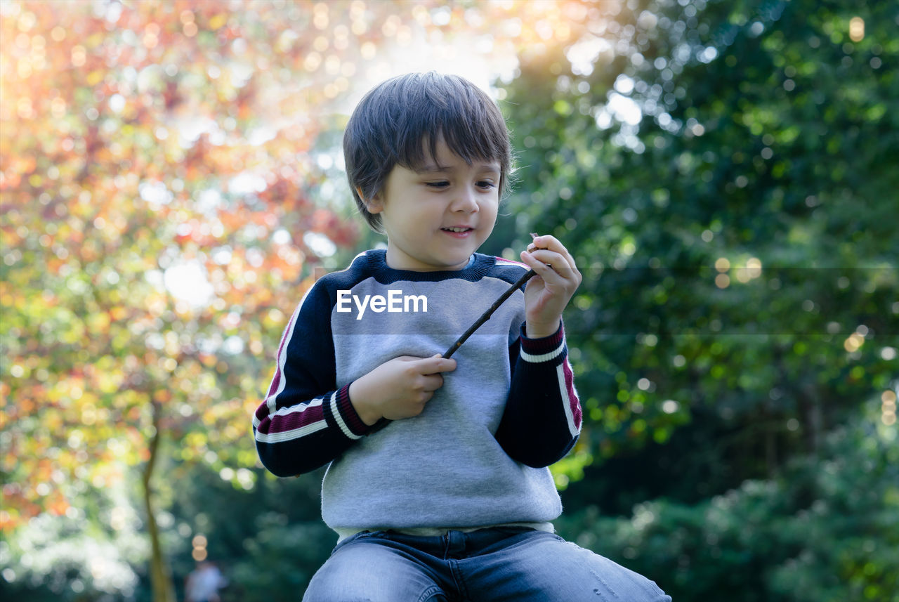 side view of boy standing against tree