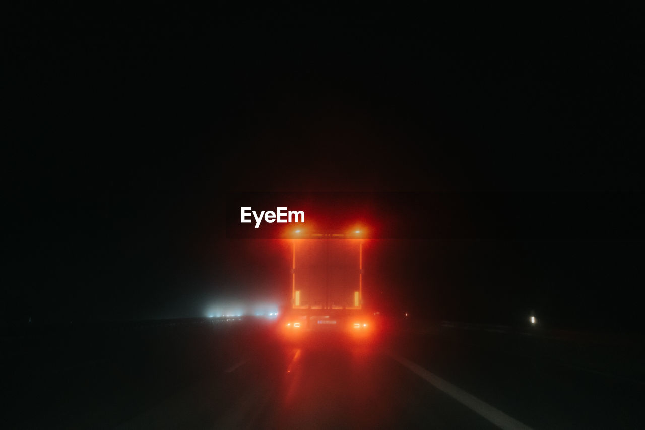 LIGHT TRAILS ON ROAD AGAINST ILLUMINATED BUILDING AT NIGHT