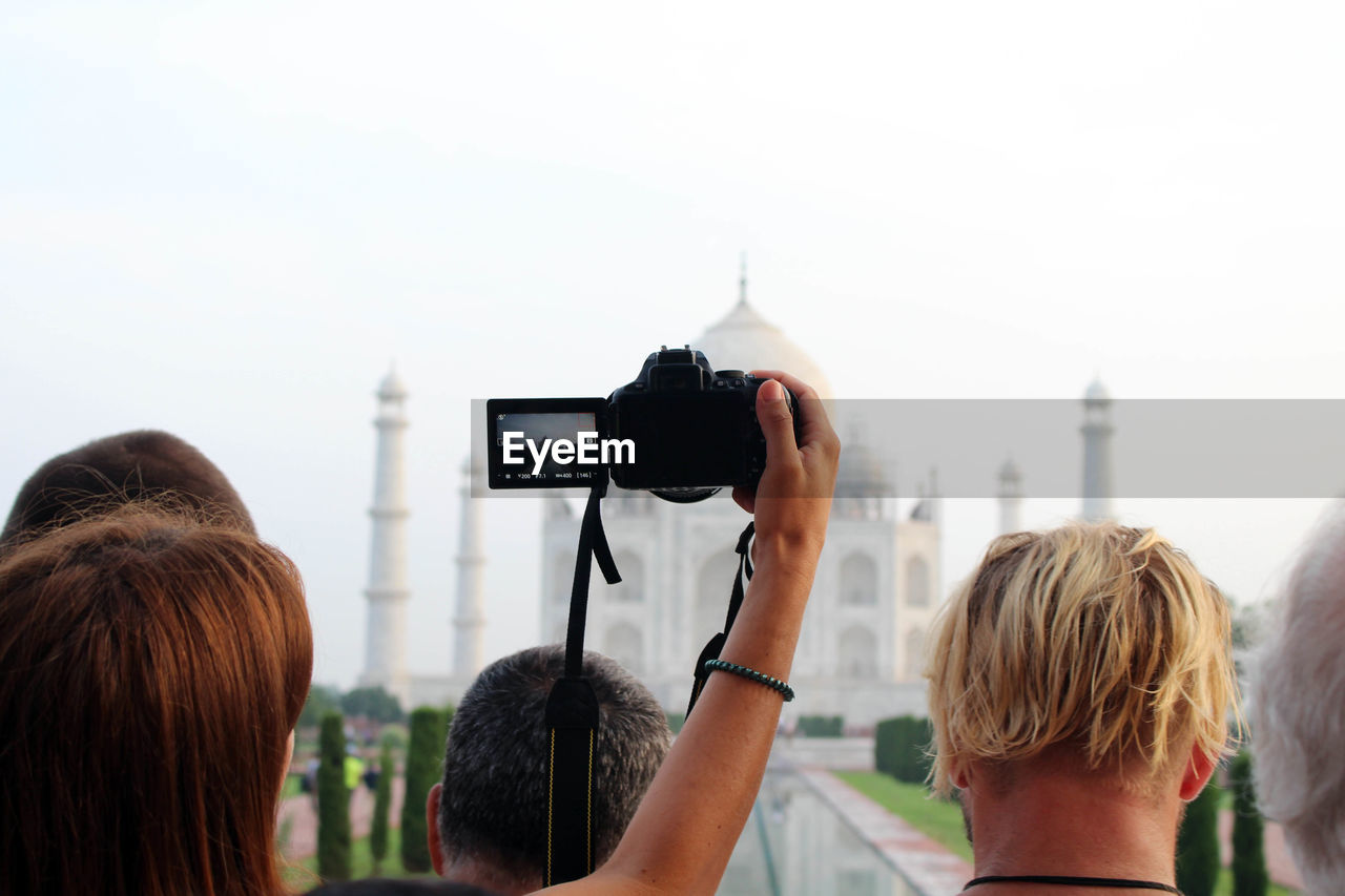 REAR VIEW OF WOMAN PHOTOGRAPHING AGAINST SKY