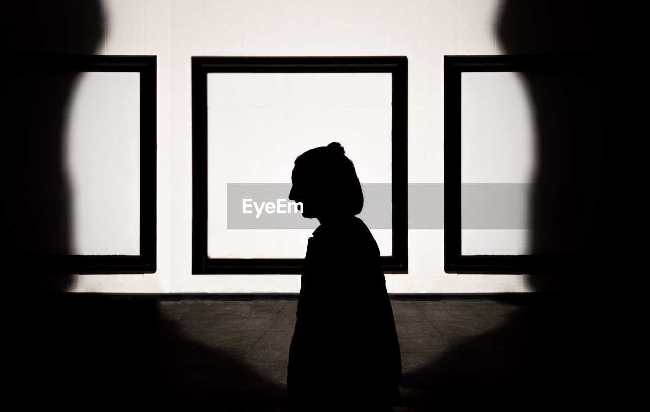 SIDE VIEW OF SILHOUETTE WOMAN STANDING AGAINST WINDOW