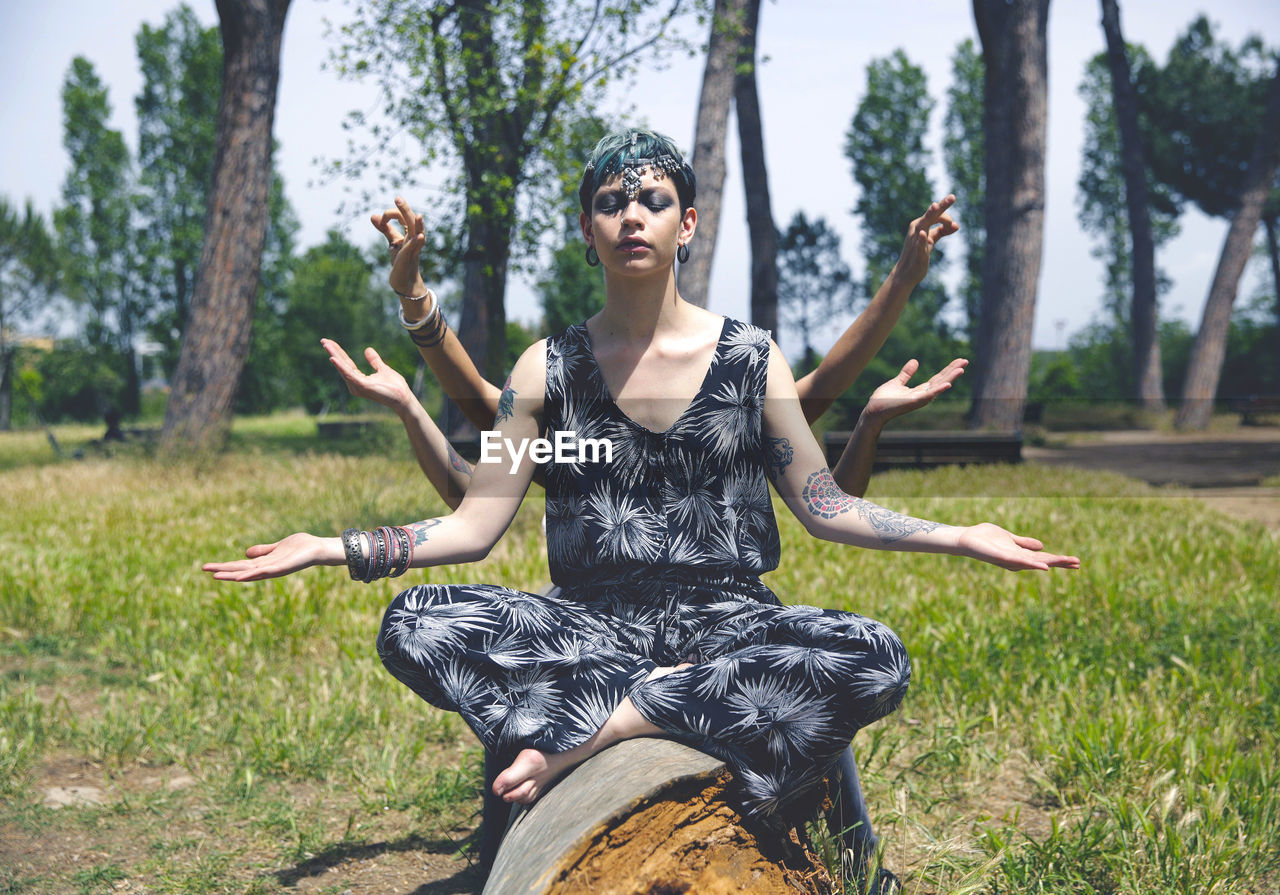 Young woman gesturing mudra while sitting on fallen tree