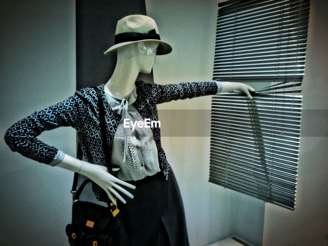 Mannequin wearing jacket and hat with shoulder bag holding blinds at shop
