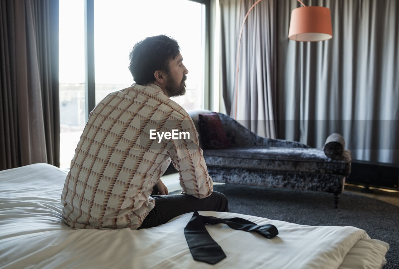 Rear view of businessman sitting on bed in hotel room