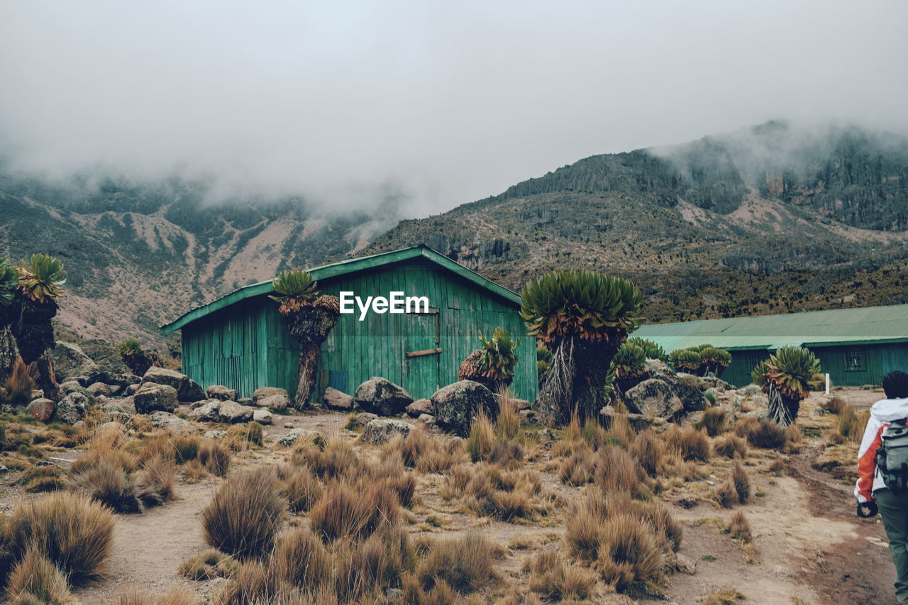 House on field by mountain against sky