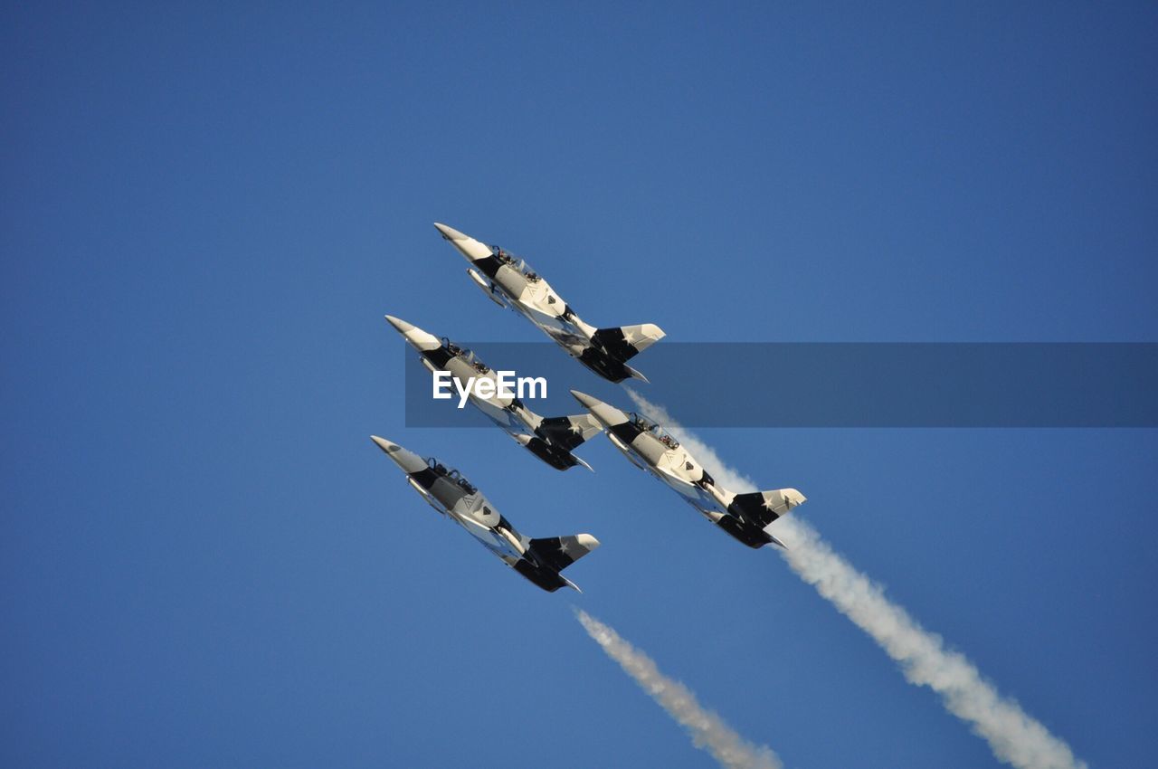 Low angle view of military aircrafts with trails against clear blue sky