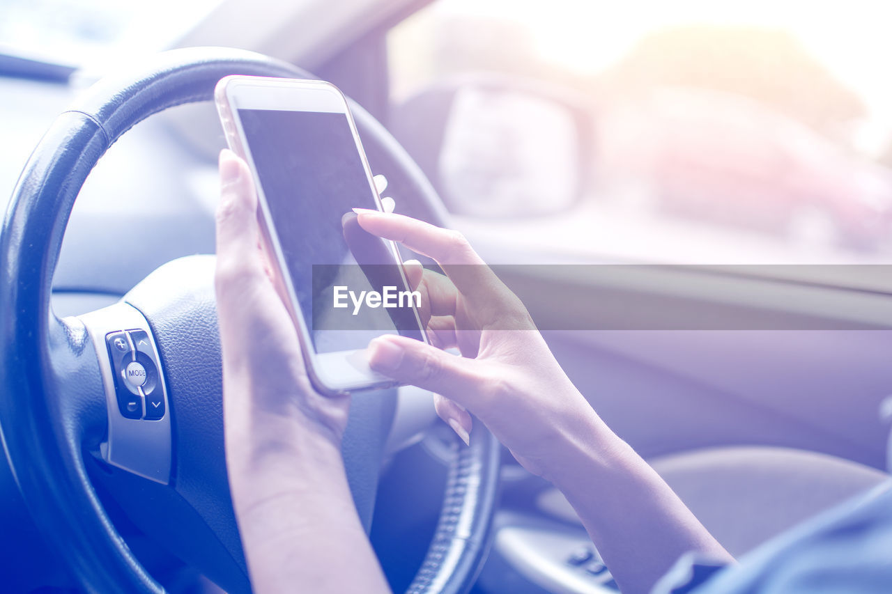 Cropped hand of woman using mobile phone in car