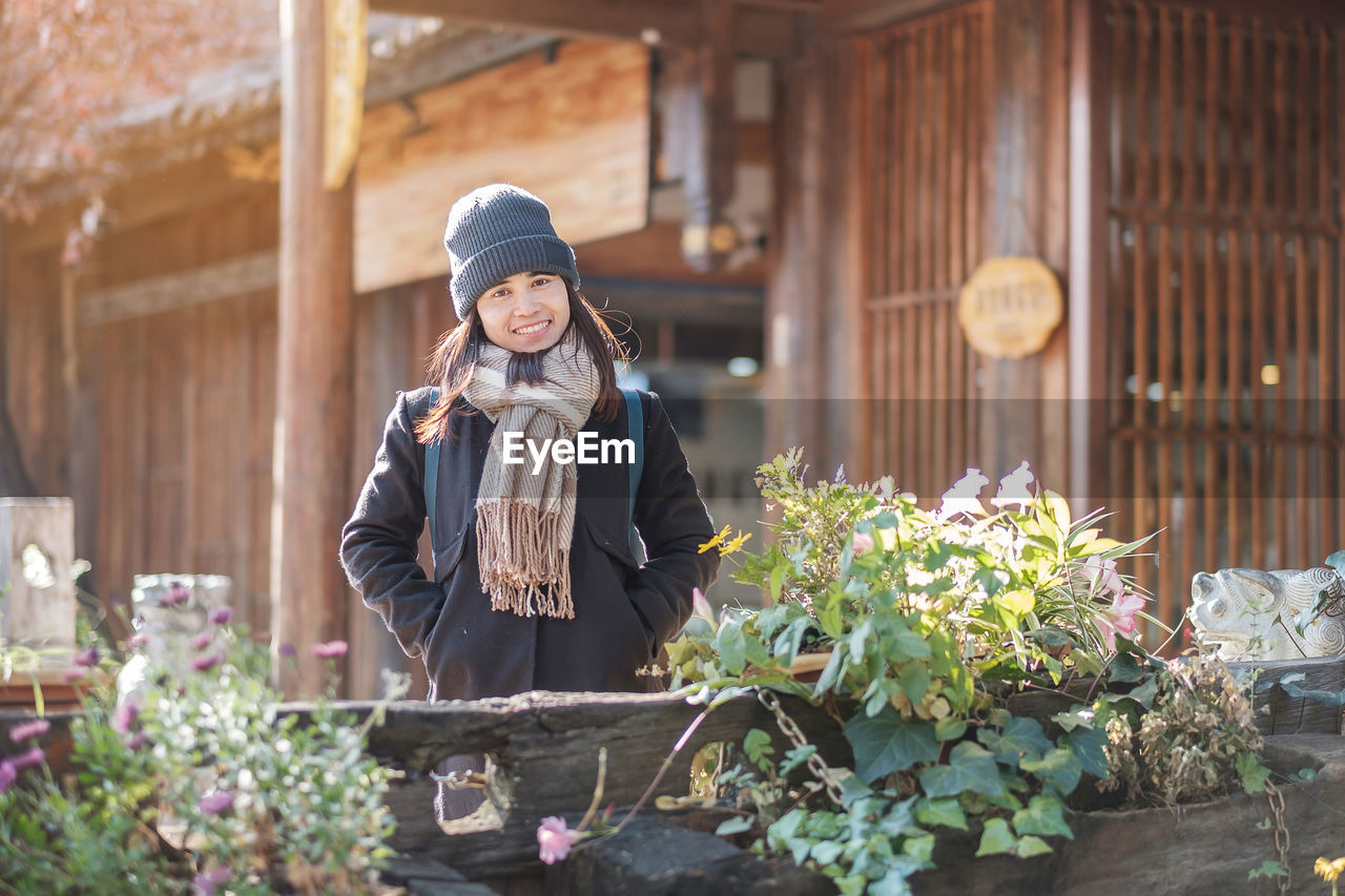 FULL LENGTH OF WOMAN STANDING BY FLOWERING PLANT