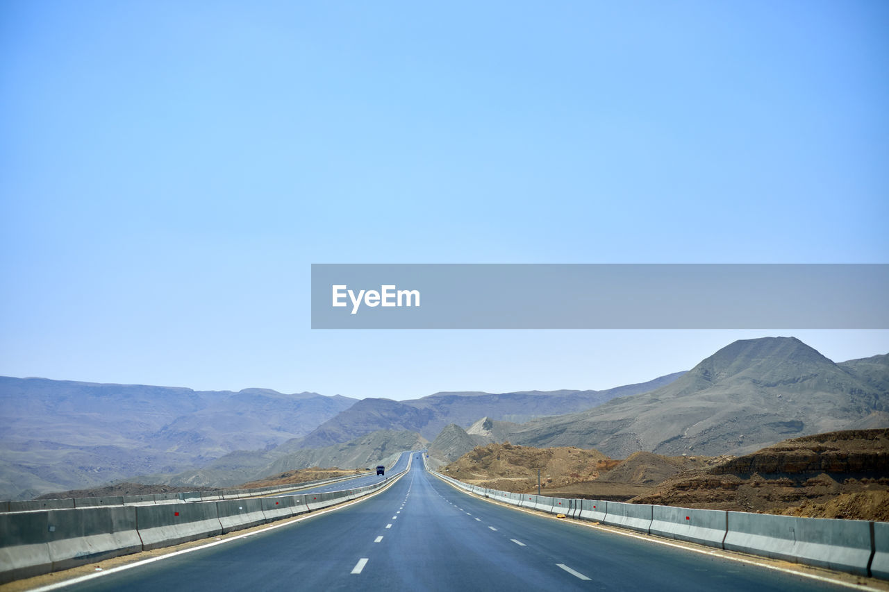 Empty road along landscape against clear blue sky