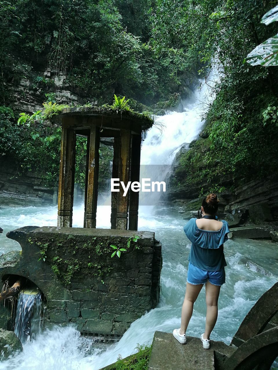 Rear view of woman standing against waterfall in forest