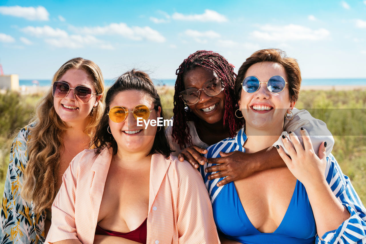 portrait of happy friends wearing sunglasses against sky