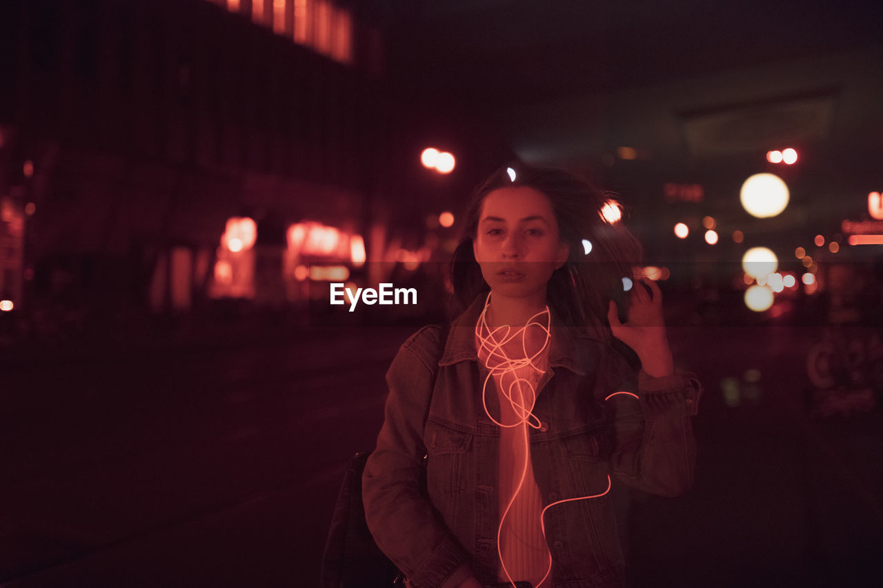 Portrait of young woman standing on road at night