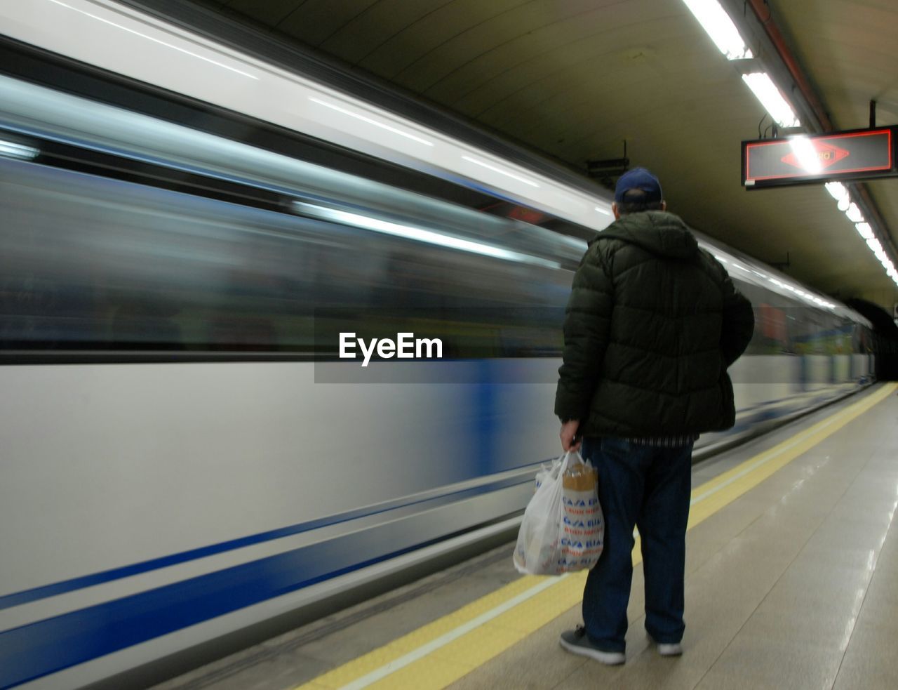 REAR VIEW OF MAN WALKING ON RAILROAD STATION PLATFORM