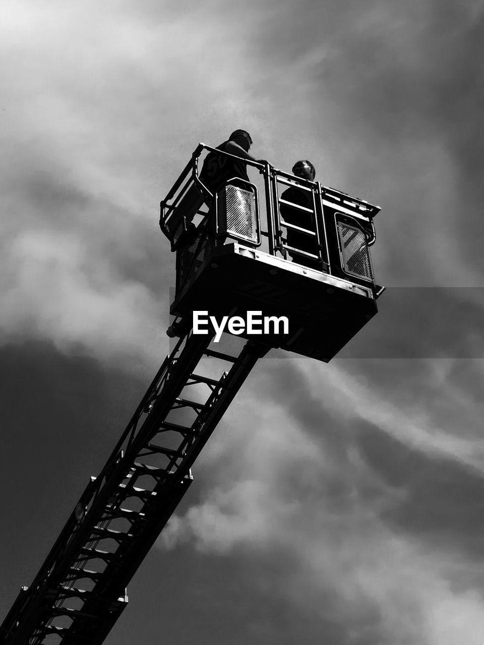 Low angle view of men standing on crane against sky
