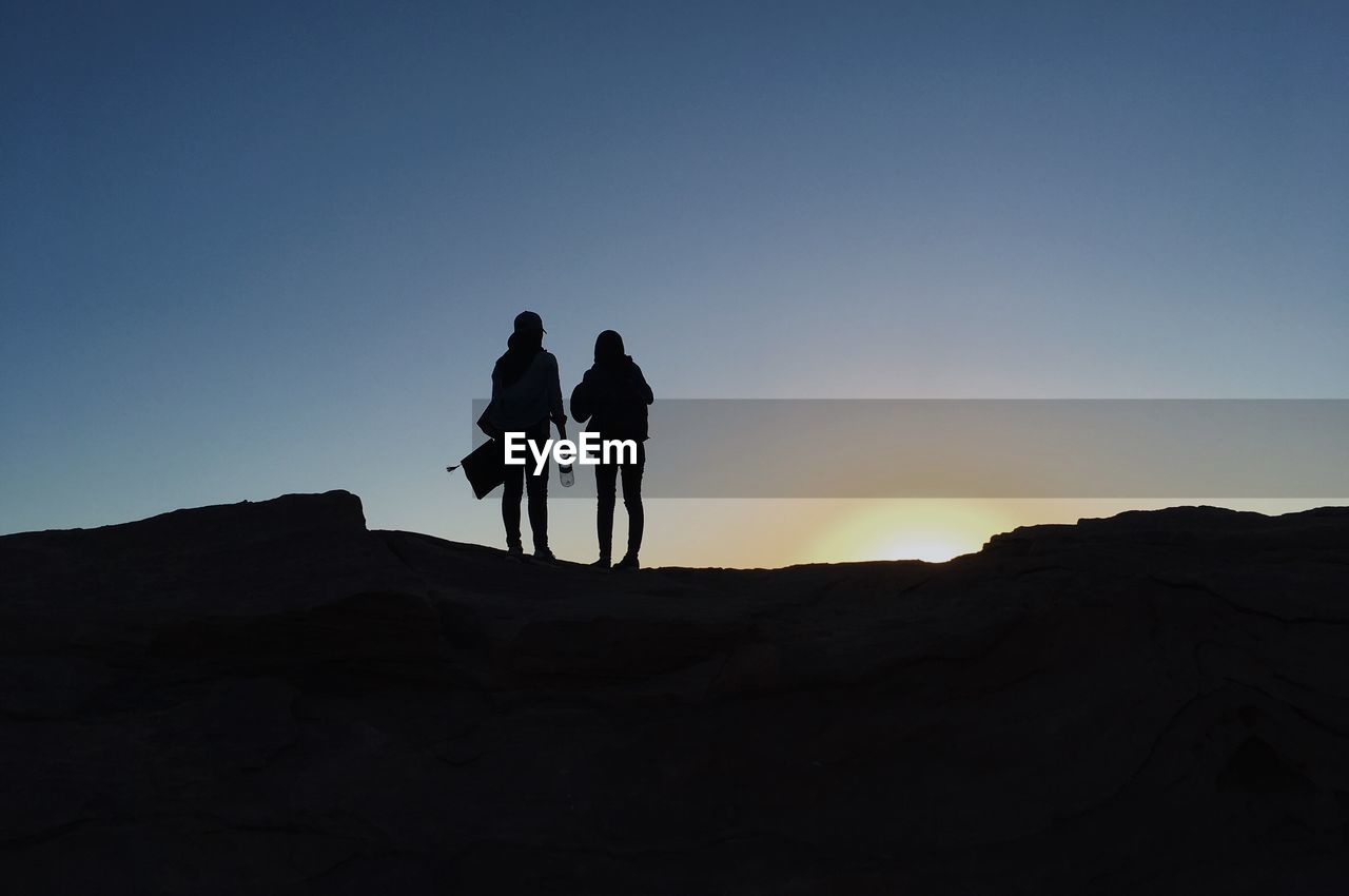 Silhouette friends standing on rock at sunset