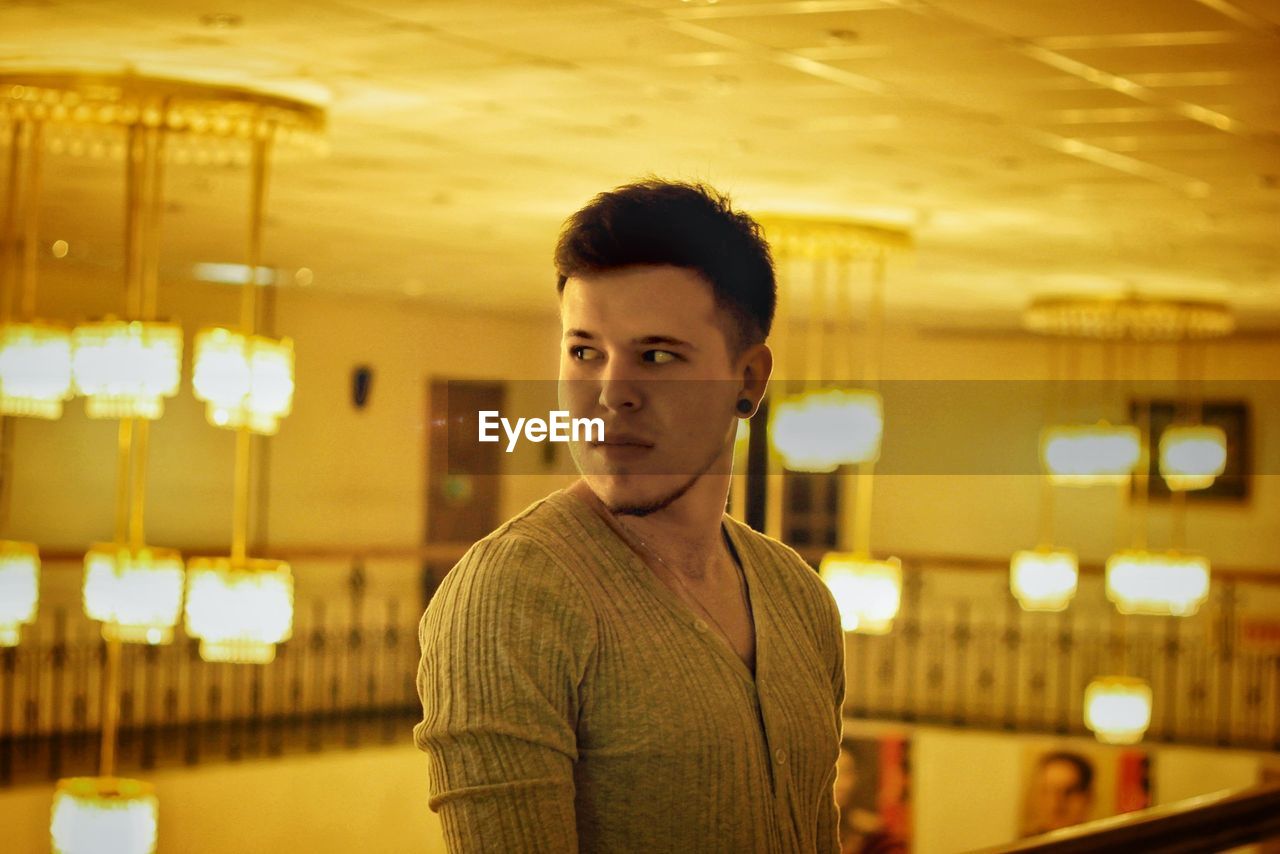 Young man looking away while standing indoors