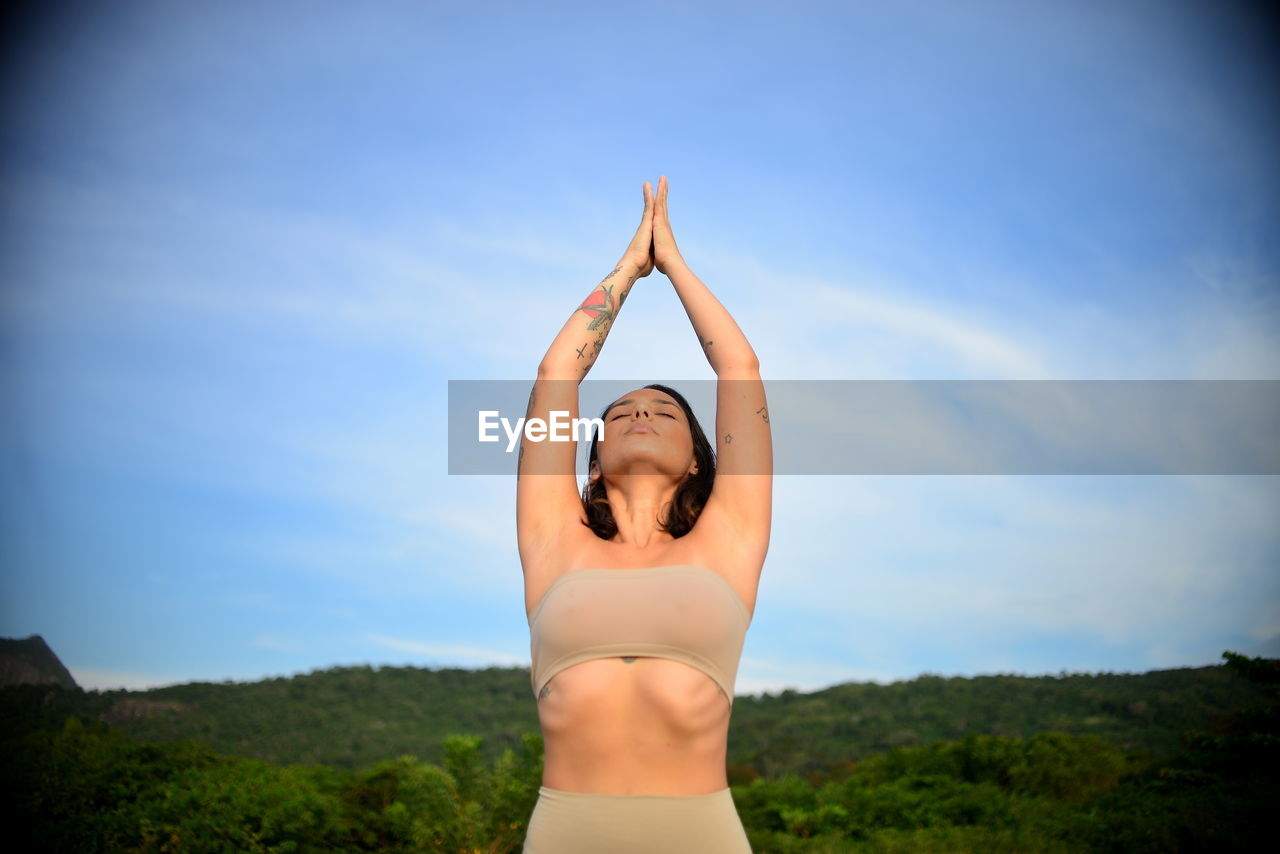 Beautiful woman meditating against sky