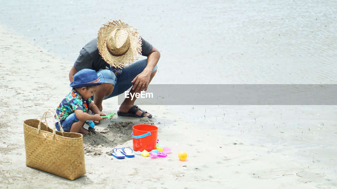 Father and son playing with toy on sand at beach