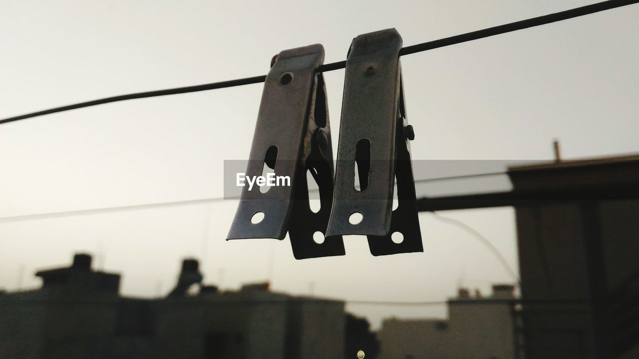 Close-up of clothespins hanging on rope against sky