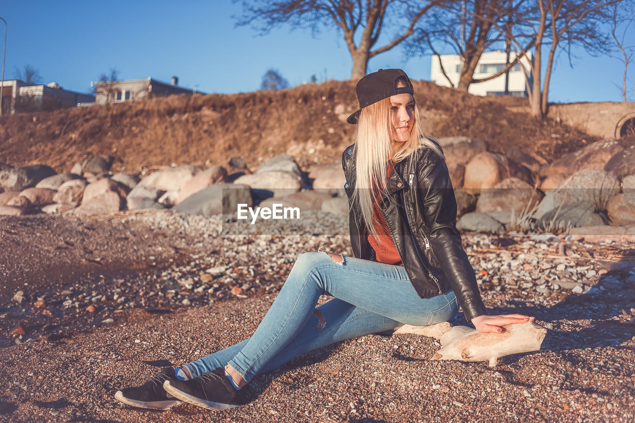 Portrait of smiling young woman sitting on rock against sky