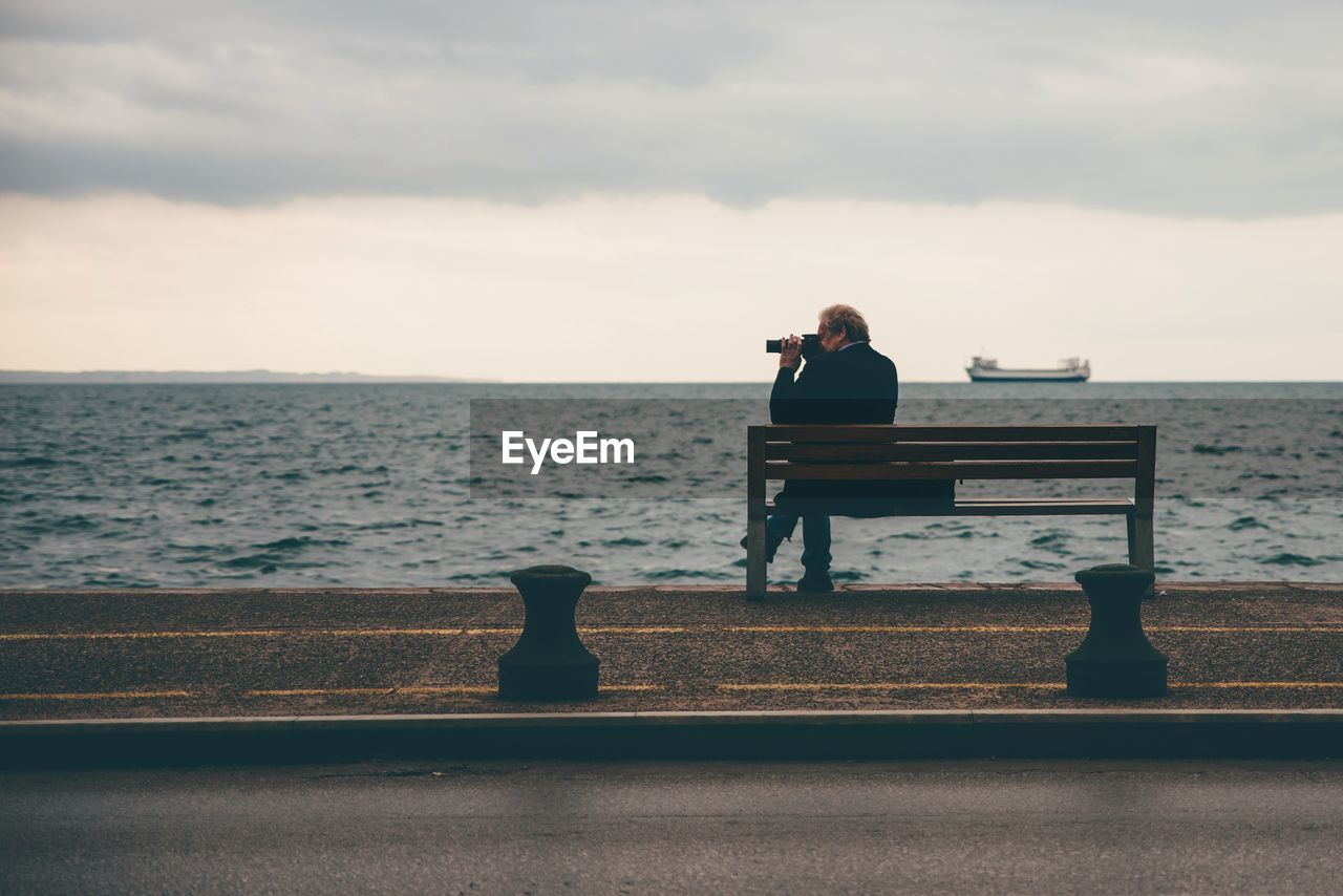 Man photographing at beach against sky