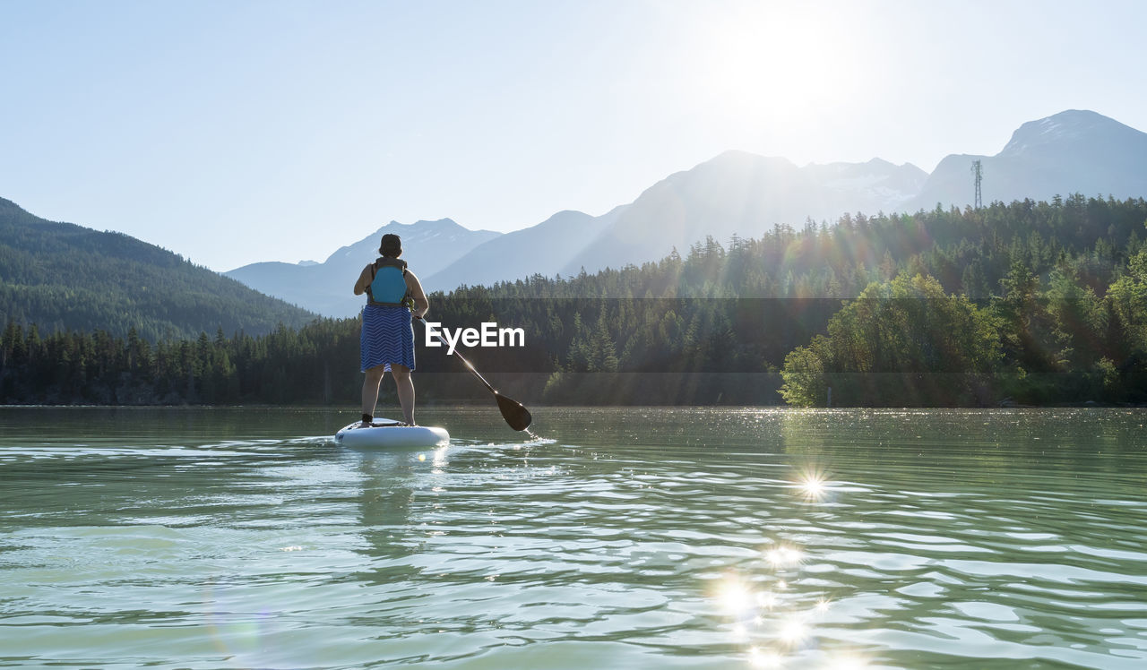 Anonymous female paddleboarding on sunny day on mountain lake