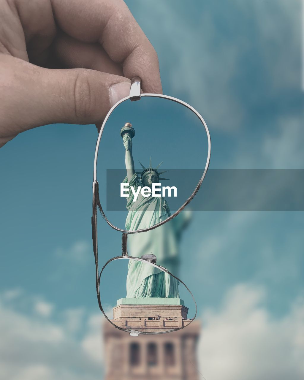 Cropped hand holding eyeglasses against statue of liberty