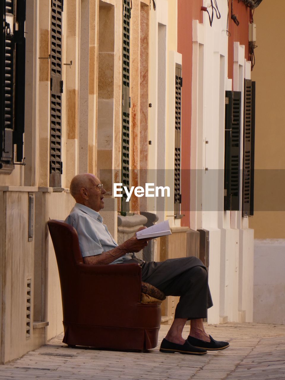 MAN SITTING ON SEAT AGAINST BUILDING