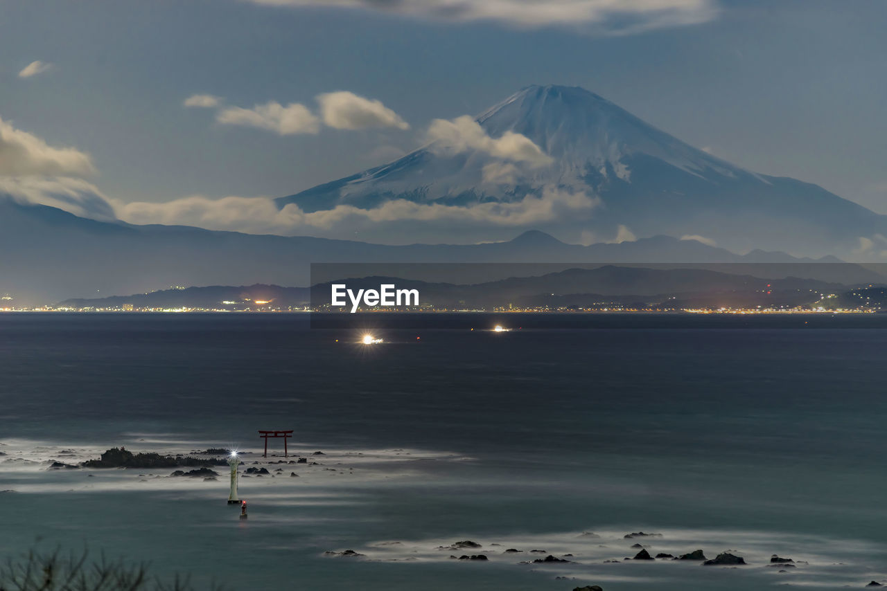 Scenic view of sea by snowcapped mountains against sky