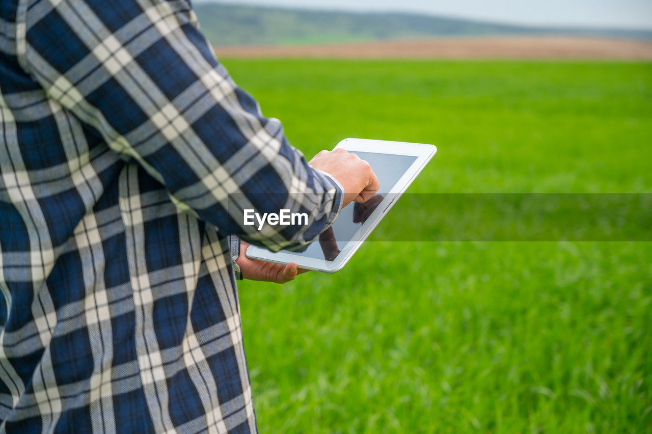 midsection of man using digital tablet while standing on field