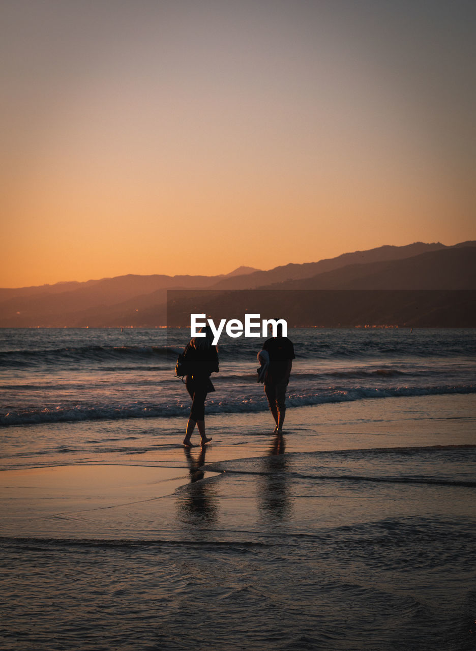 Full length of couple on beach against sky during sunset