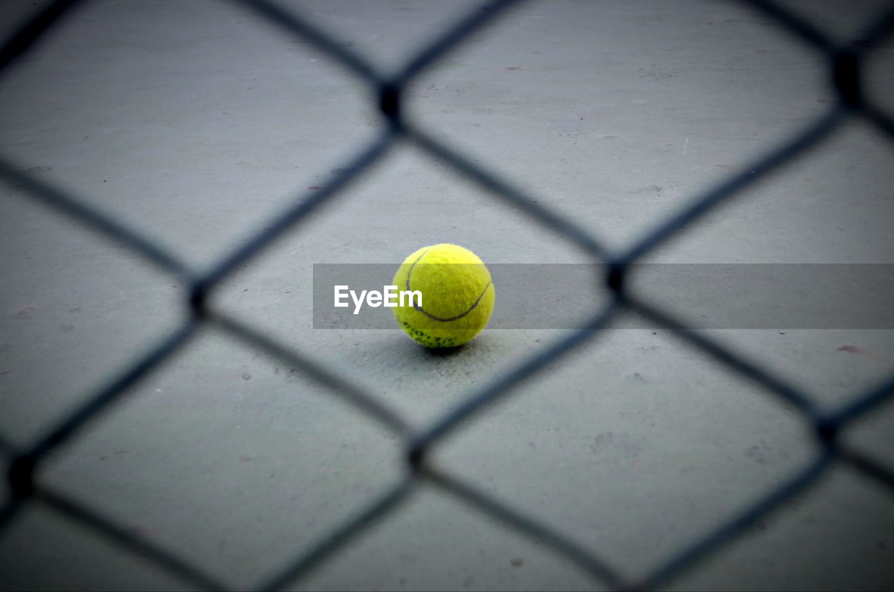 Close-up of yellow ball on floor seen through chainlink fence