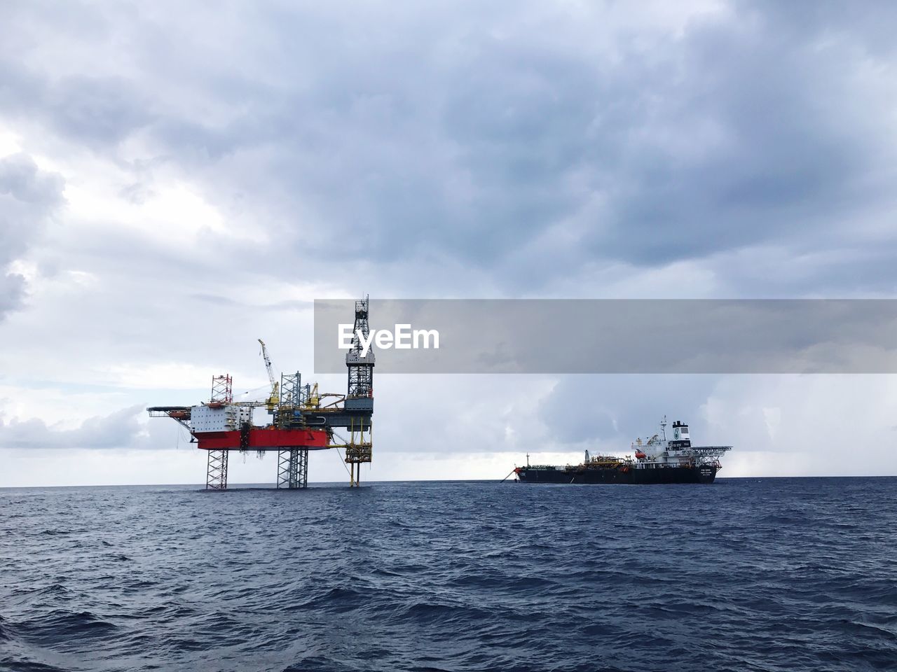 Ship by oil rig in sea against sky