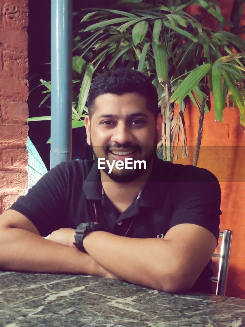 portrait, one person, smiling, looking at camera, young adult, sitting, adult, happiness, person, front view, casual clothing, men, lifestyles, photo shoot, emotion, leisure activity, relaxation, plant, nature, cheerful, clothing, day, smile, teeth, outdoors, leaning, architecture, beard, headshot, human face