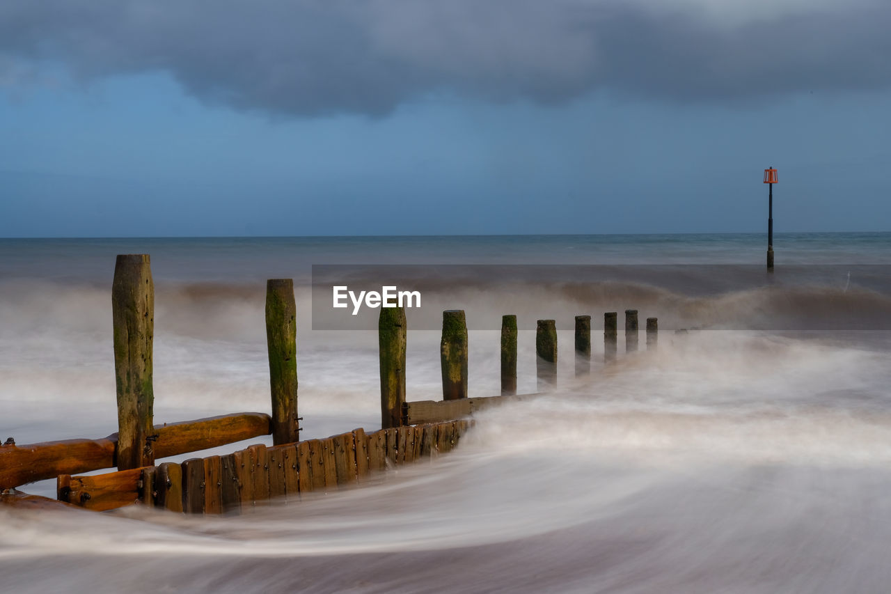 Wooden posts on beach against sky