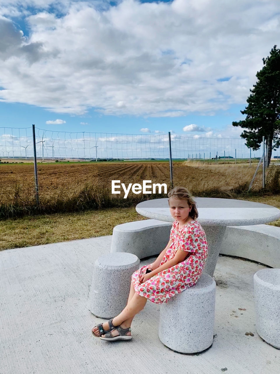 Full length portrait of girl sitting against sky