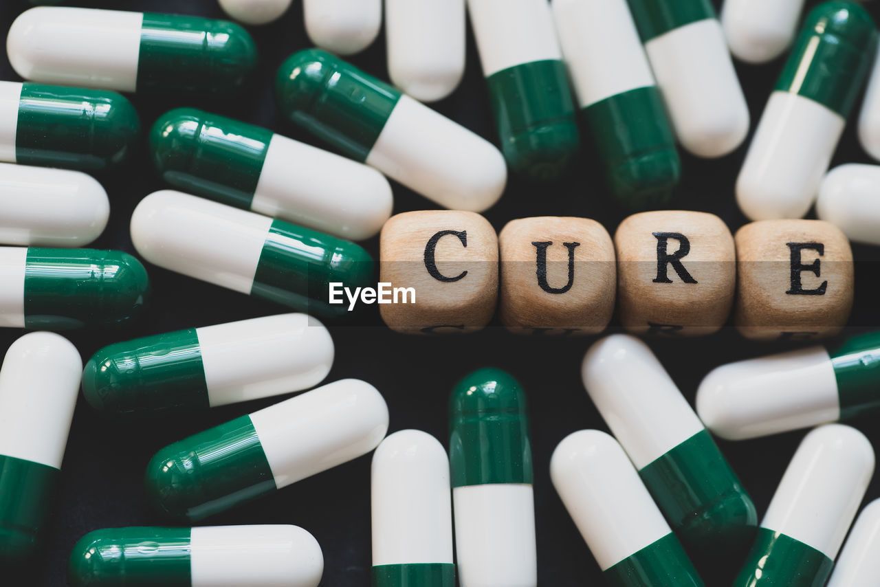 Cure word on wooden alphabet block with green pills as the background.