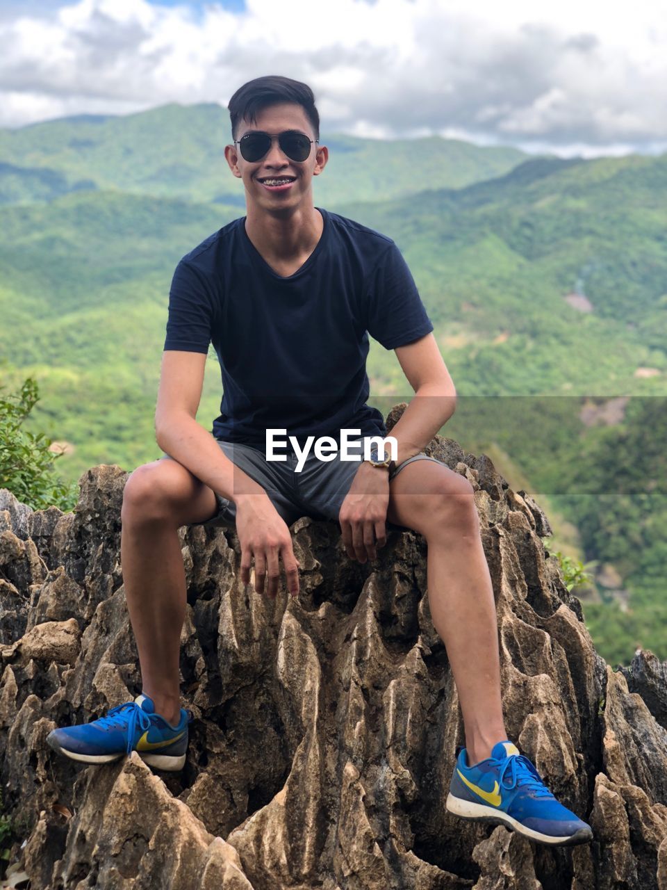 FULL LENGTH PORTRAIT OF YOUNG MAN SITTING ON ROCKS