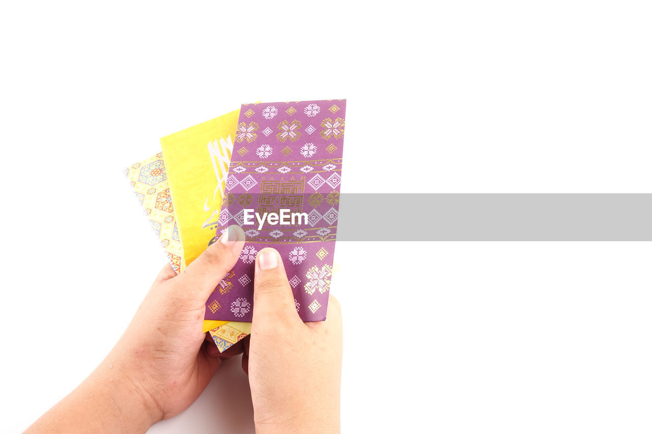 Close-up of woman hand holding multi colored envelope against white background