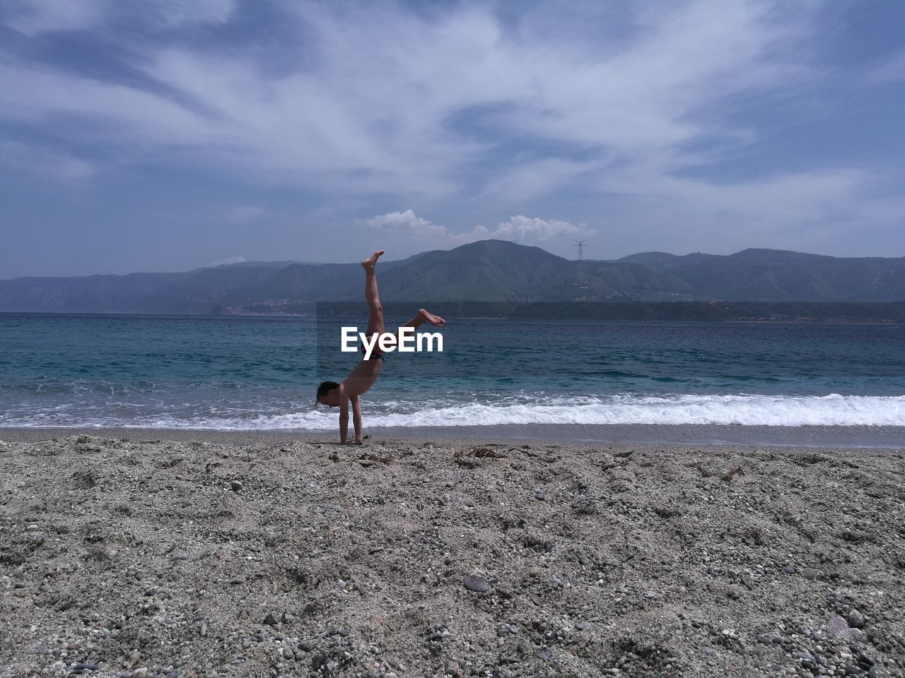 Boy practicing cartwheel at beach against sky