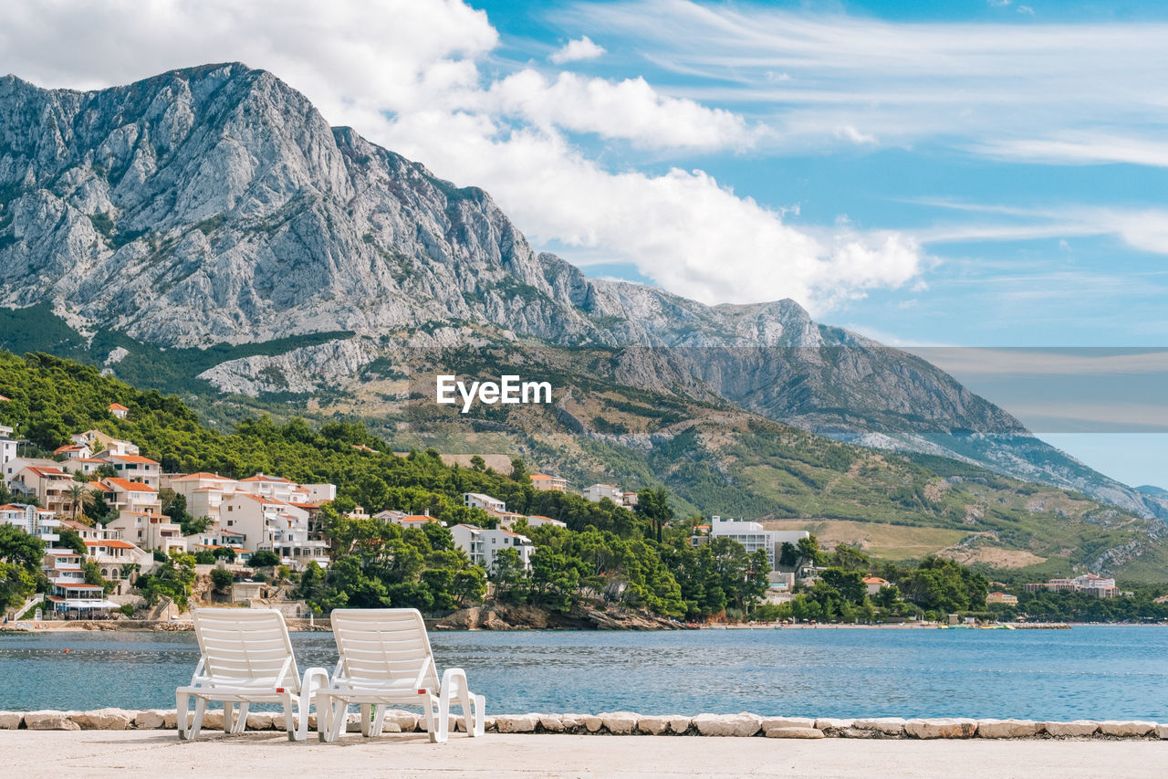 Deck chairs at beach against scenic view of sea and biokovo mountains