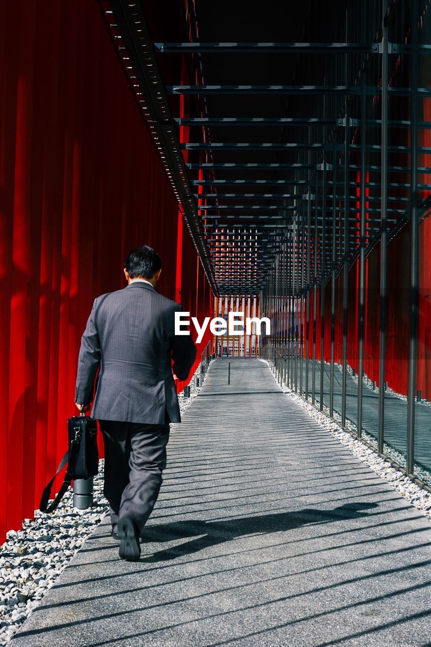 FULL LENGTH REAR VIEW OF MAN WALKING IN RED OFFICE