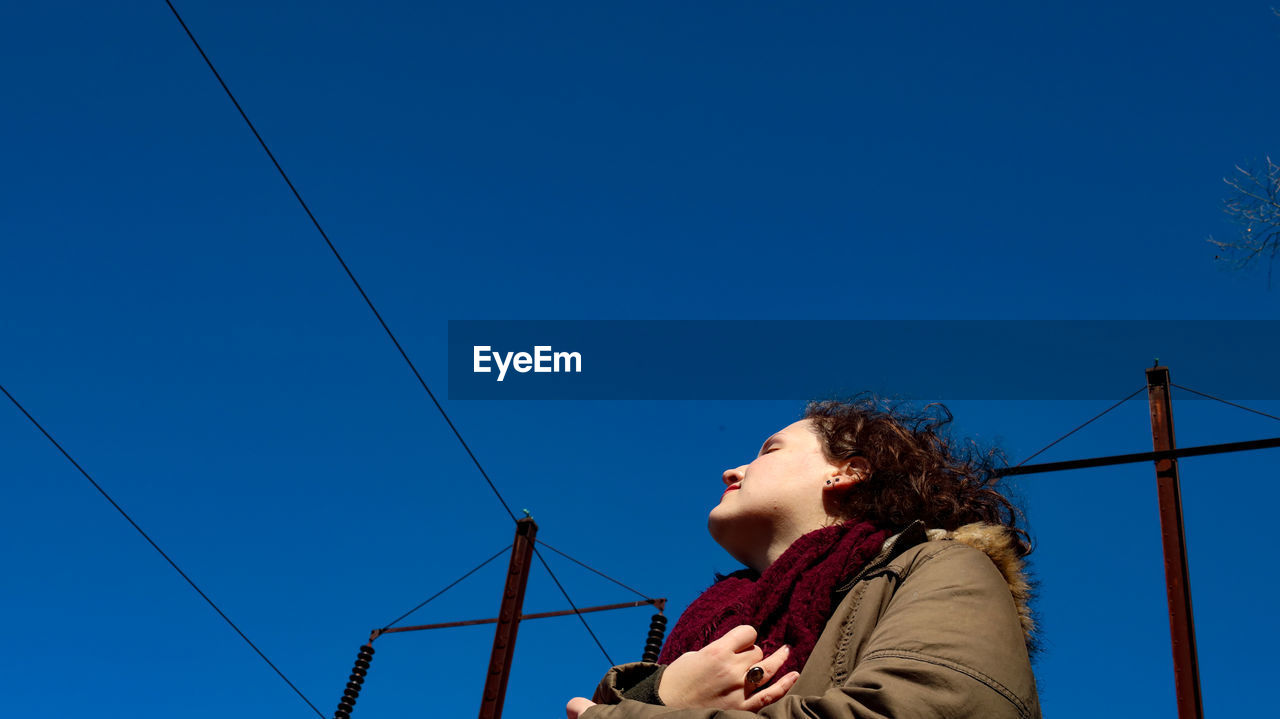 Low angle view of girl looking away against blue sky