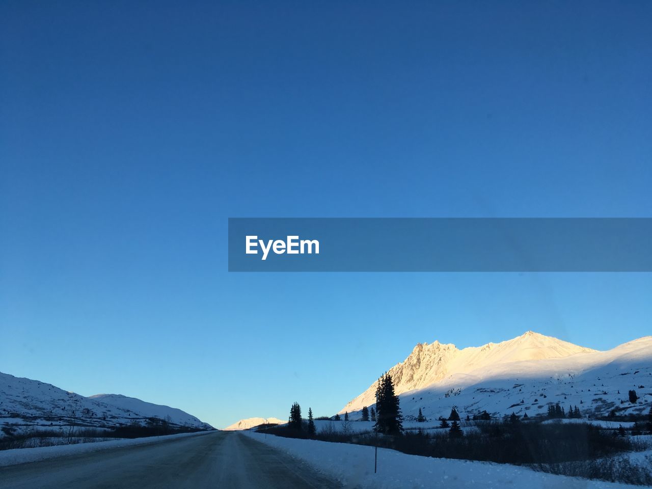 ROAD BY SNOWCAPPED MOUNTAIN AGAINST CLEAR BLUE SKY