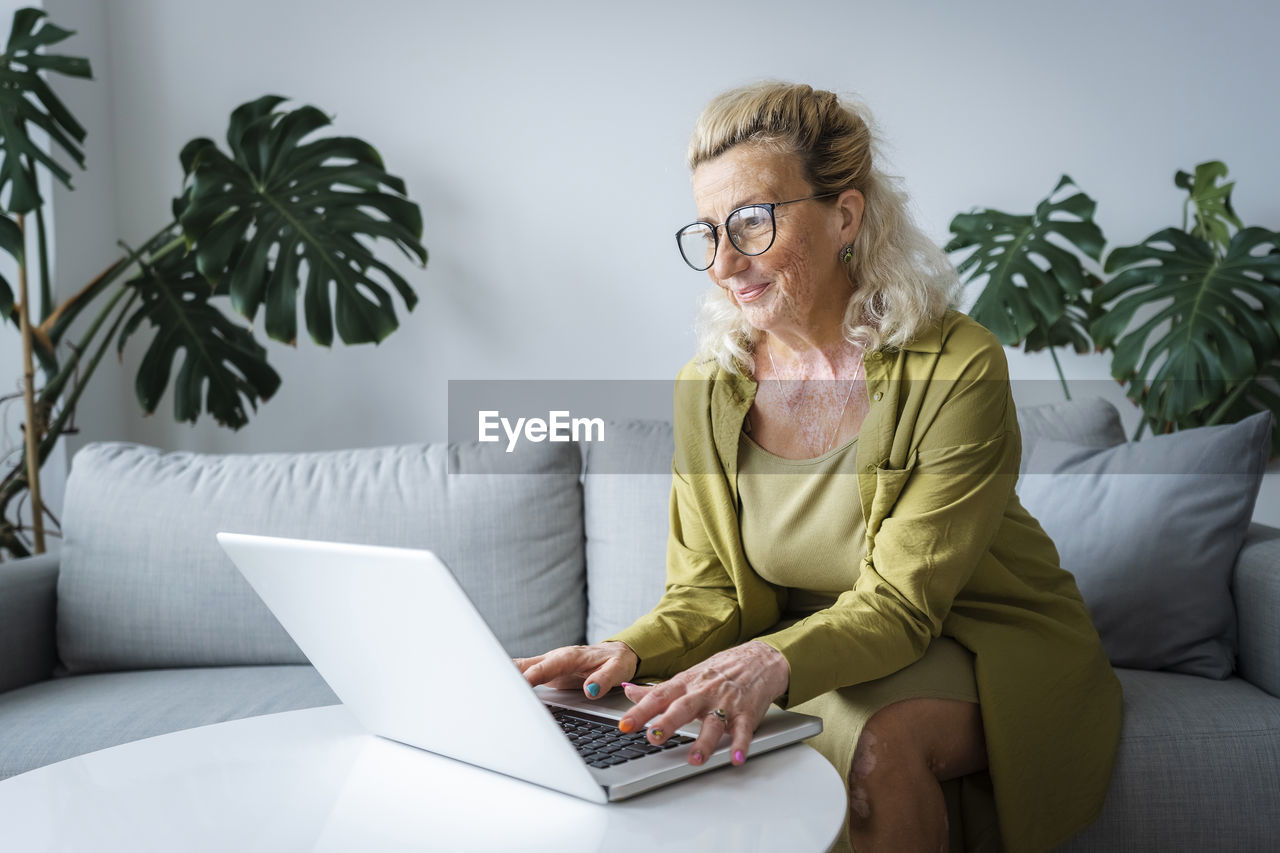 Happy elderly freelancer working on laptop sitting at home