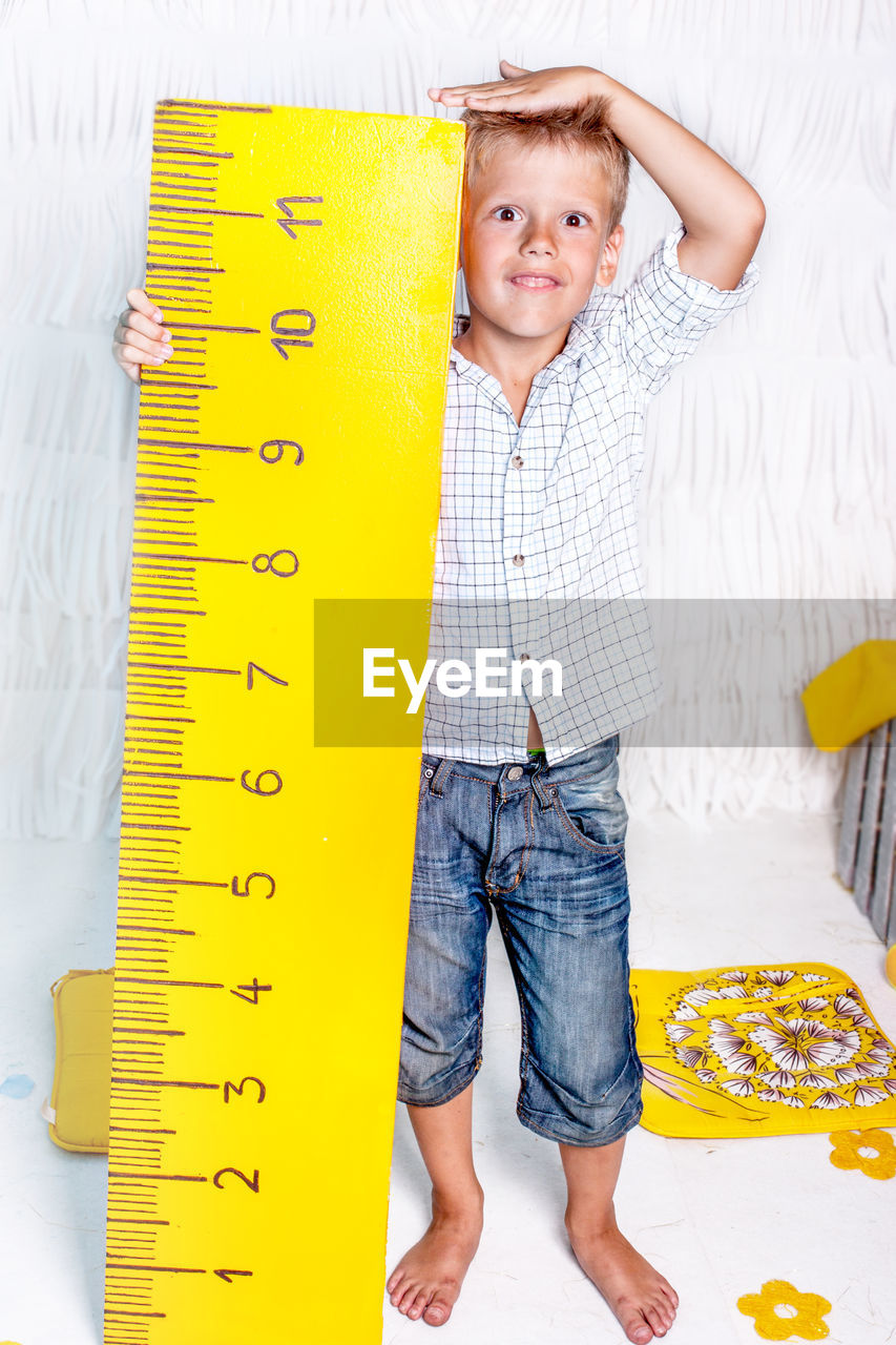 Portrait of cute smiling boy measuring height at home