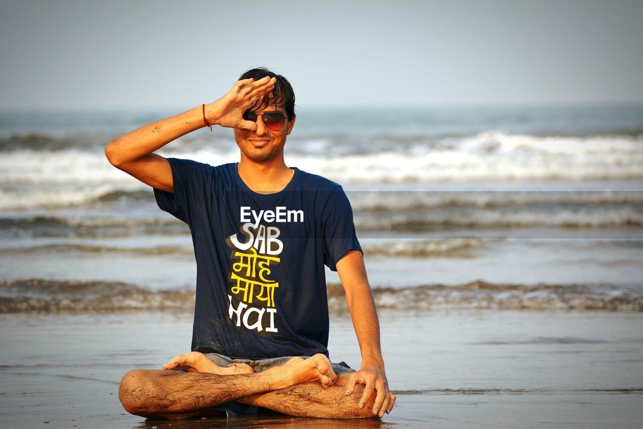 Full length of wet young man practicing yoga at beach