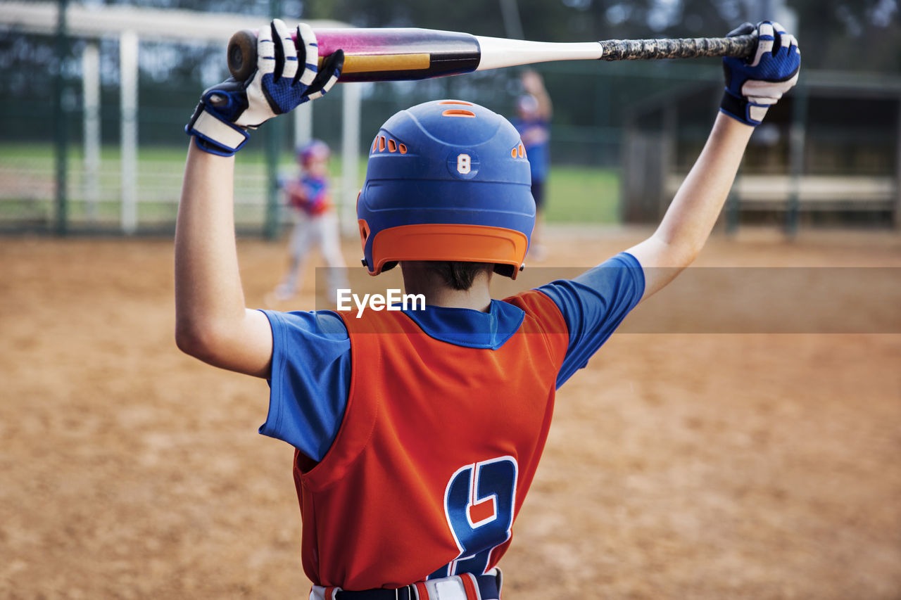 Rear view of boy holding baseball bat on field