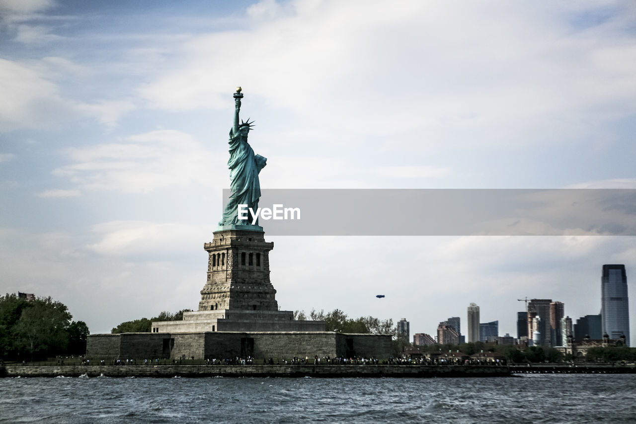 Low angle view of statue of liberty in city against cloudy sky