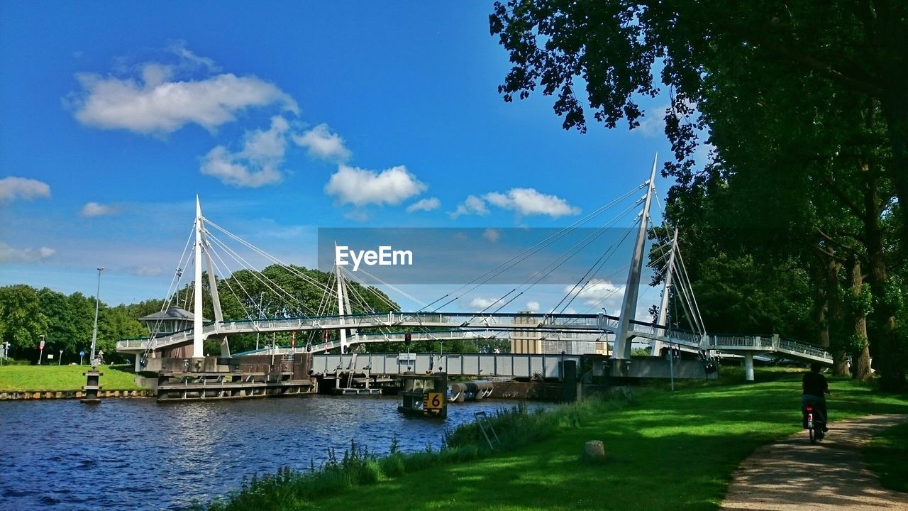 Bridge over canal by grassy field against cloudy sky